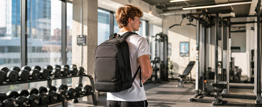 A black VGCUB backpack worn on the shoulders, seen from behind in a gym